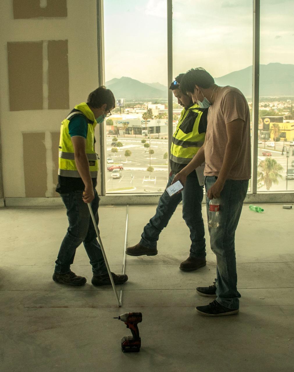 Personal revisando niveles de piso en obra con chalecos de seguridad
