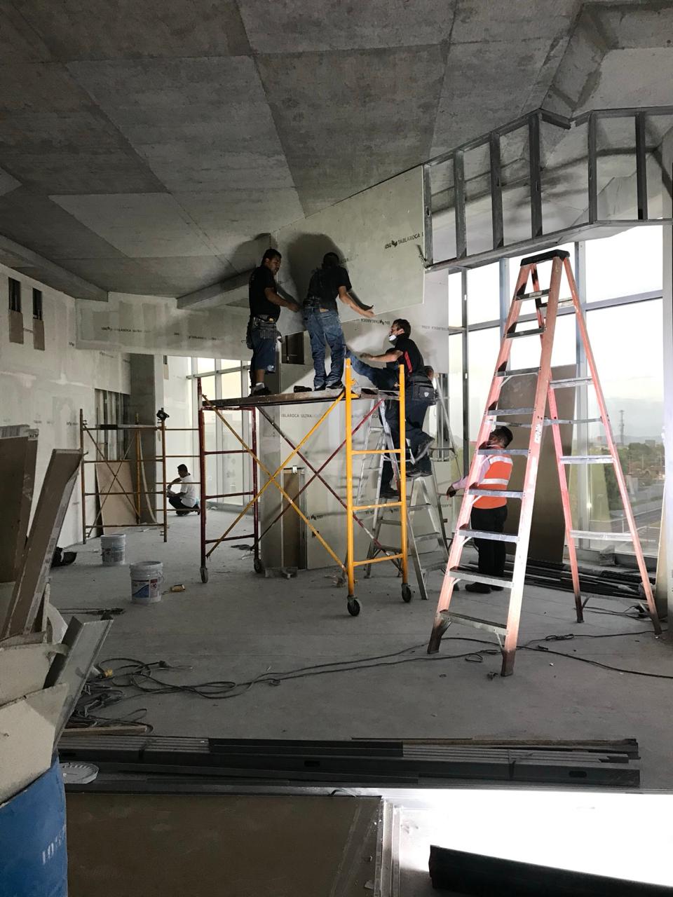 Instalación de tablaroca sobre andamios junto al muro cortina