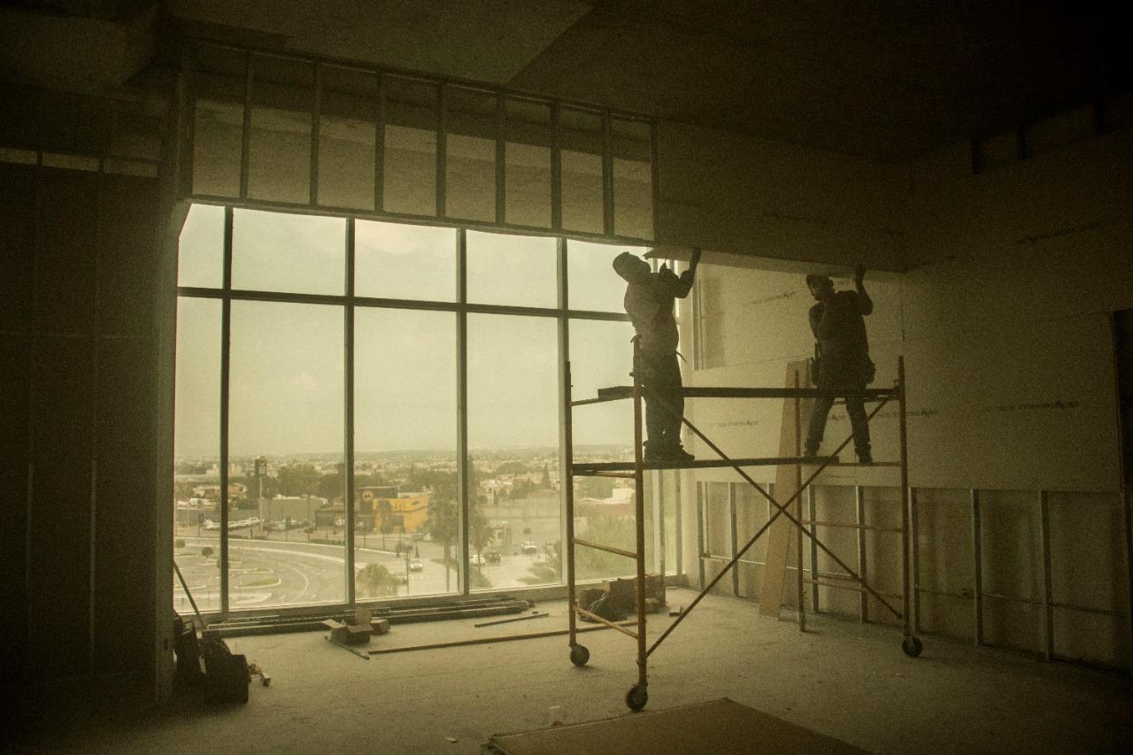 Soldadores sobre andamio instalando muro cortina en torre de oficinas